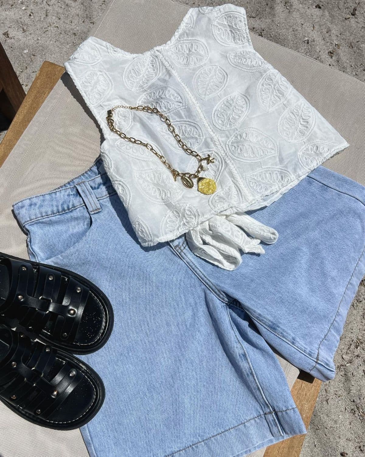 Top brodé, short en jean, sandales et collier doré posés à plat